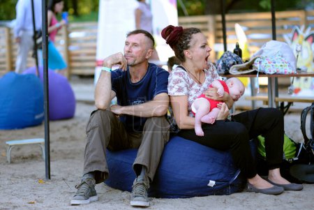 Foto de Hombre y mujer con un bebé en las manos sentados en una bolsa de frijoles, mujer bostezando aburrida. Fest Vedalife. 25 de julio de 2018. Kiev, Ucrania - Imagen libre de derechos