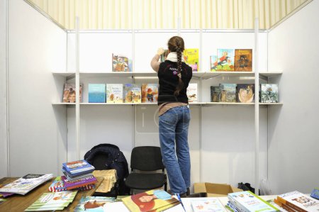 Foto de Joven librera coloca libros en las estanterías antes de abrir la librería. Feria del Libro. 14 de diciembre de 2017. Kiev, Ucrania - Imagen libre de derechos