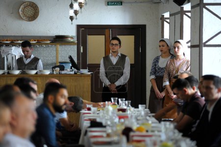 Téléchargez les photos : Restaurant tartare : serveuses en robes autochtones et gérants hommes debout près du comptoir tandis que les gens mangent aux tables. 8 septembre 2018. Kiev, Ukraine - en image libre de droit