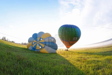Photo for Hot-air balloon drifting in the sky, car and trailer with equipment set on the ground. Pereiaslav, Ukraine - Royalty Free Image
