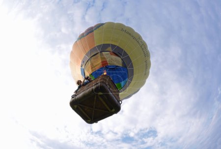 Photo for Hot-air balloon drifting in the blue sky, people aboard looking down from the basket. May 6, 2018. Pereiaslav, Ukraine - Royalty Free Image