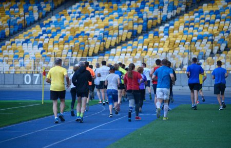 Photo for Group of people running on tracks of the stadium in the evening light. - Royalty Free Image