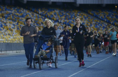 Photo for Group of people running on tracks of the stadium, in the center - woman running and pushing the wheelchair with boy with special needs (cerebral palsy). October 14, 2019. Kiev, Ukraine - Royalty Free Image