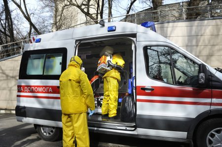 Foto de Paramédicos desinfectando el coche ambulancia con el atomizador de la mochila motorizada y el pulverizador - Imagen libre de derechos