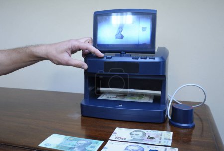 Foto de Mano de hombre encendiendo el detector de dinero, billete colocado en el receptor. Kiev, Ucrania - Imagen libre de derechos