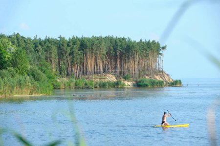 Photo for Wooded promontory, people sunbathing riding Sup boards on the water of the big river. July 20, 2021. Place near Pereyaslav-Khmelnytsky, Ukraine - Royalty Free Image