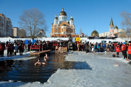 Téléchargez les photos : Foule de personnes plongeant dans le trou glacé et debout sur une rive de la rivière où la fête de l'Épiphanie a eu lieu, église sur un fond. 19 janvier 2019. Kiev, Ukraine - en image libre de droit