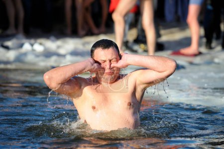 Téléchargez les photos : Baptême. Jeune homme pincer le nez avant de plonger dans le trou d'eau froide pendant la fête Epiphanie sur la rivière, les jambes des gens sur un fond. 19 janvier 2019. Kiev, Ukraine - en image libre de droit