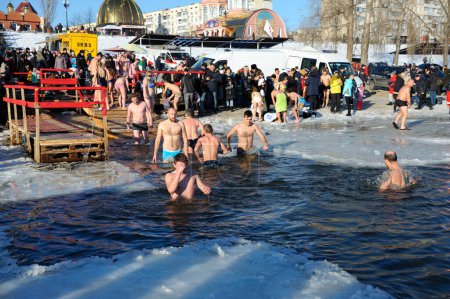 Téléchargez les photos : Foule de personnes plongeant dans le trou glacé et debout sur une rive de la rivière où la fête de l'Épiphanie a eu lieu, église sur un fond. 19 janvier 2019. Kiev, Ukraine - en image libre de droit