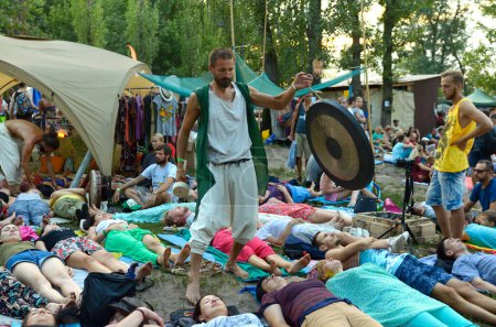 Foto de Gente acostada en karemats y meditando, hombre monje tocando gong instrumento musical. Festival Vedalife. 7 de agosto de 2017. Kiev, Ucrania - Imagen libre de derechos