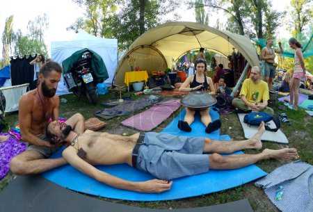Foto de Instructor haciendo masajes al hombre acostado en karemat, gente relajándose alrededor del campamento del festival. Festival Vedalife. 7 de agosto de 2017. Kiev, Ucrania - Imagen libre de derechos
