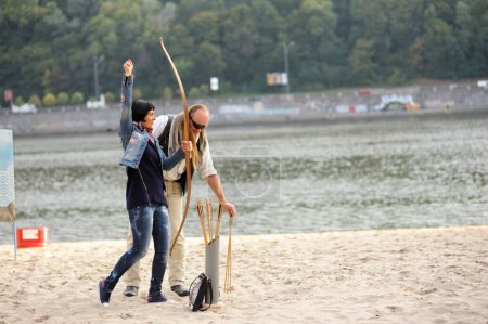 Téléchargez les photos : Un archer enseignant le tir à l'arc jeune femme sur la plage de sable de la rivière, flèches, carquois et arc. 11 novembre 2019. Kiev, Ukraine - en image libre de droit