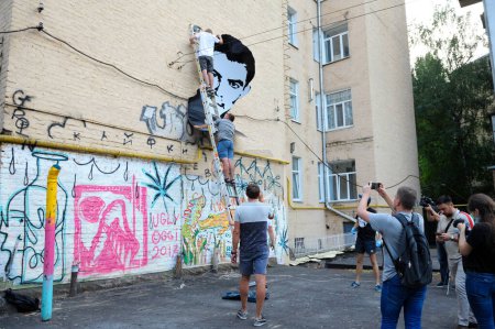 Photo for Young men activists set the poster portrait of famous Ukrainian poet and dissident Vasyl Stus on the wall of the building. June 12, 2018. Kyiv, Ukraine - Royalty Free Image