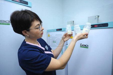 Lab assistant holding breast milk storage containers with human milk inside, freezers on a background. April 12, 2019. Kiev, Ukraine