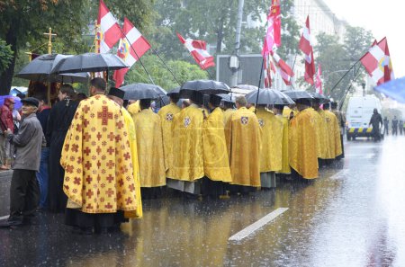 Photo for Orthodox priests in golden cassocks standing on a street under rain using umbrellas before Ukrainian Orthodox Church of Kyiv Patriarchate cross procession. July 28, 2019. Kyiv, Ukraine - Royalty Free Image