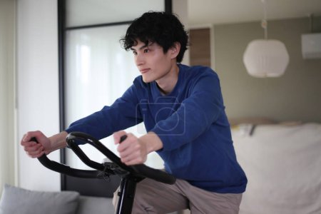 Téléchargez les photos : Homme utilisant vélo de fitness à la maison - en image libre de droit