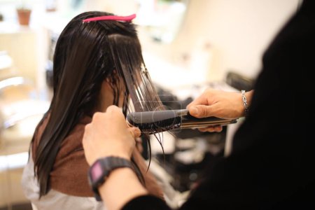 Téléchargez les photos : Coiffeur masculin appliquant du fer à friser sur les cheveux de la femme - en image libre de droit