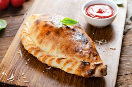 Photo for Delicious Pizza Calzone, Traditional Italian Pizza with Tomatoes and Fresh Basil on Wooden Rustic Background - Royalty Free Image