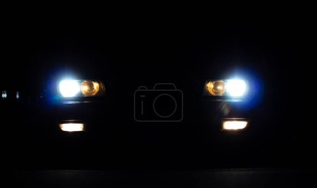 Headlights of a European car glowing from the darkness.