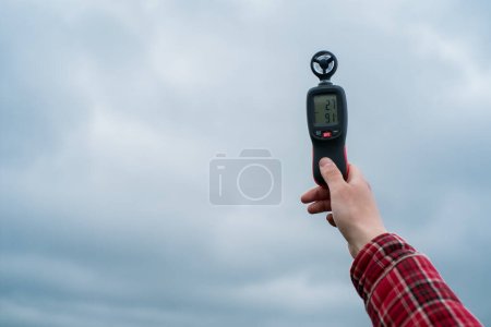 un agricultor sostiene en su mano un instrumento para medir la velocidad del viento sobre el fondo del cielo