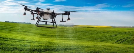 Téléchargez les photos : Un drone pulvérisateur survole une colline de champs avec du blé d'hiver. Agriculture intelligente Application de Zzr par drones - Application ponctuelle pour augmenter le rendement - en image libre de droit