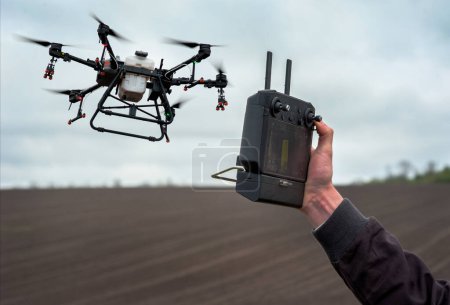 Foto de Las manos masculinas sostienen el control remoto de un dron pulverizador agrícola establece los límites del campo para la pulverización - Imagen libre de derechos