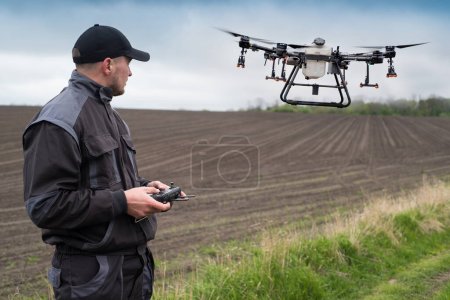 Téléchargez les photos : Opérateur d'un drone agricole avec télécommande, commande de drone pour la pulvérisation sur le terrain - en image libre de droit
