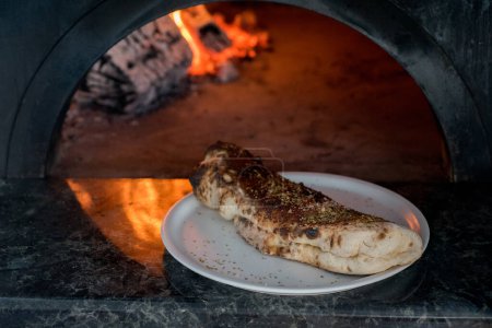 calzone pizza on a plate close-up, Neapolitan traditional wood-burning oven with burnt edges in the background