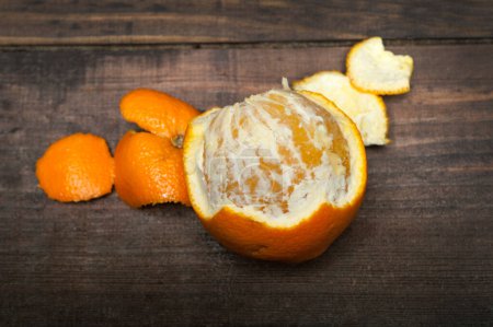Photo for Close-up texture of an peeled ripe sweet tangerine fruit. Top view of tangerine orange partly peeled on a wooden board. - Royalty Free Image