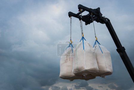 bags with seeds suspended by a crane against the background of the sky, unloading seeds or fertilizers before sowing