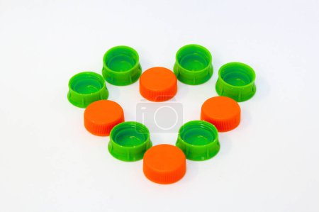 Grüne und orangefarbene Plastikflaschenverschlüsse isoliert auf weißem Hintergrund in Herzform angeordnet