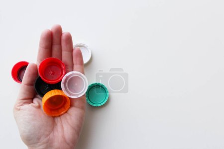 Mano de mujer sosteniendo tapas de plástico sobre fondo blanco, espacio para copia. Sostenibilidad, concepto de reciclaje para el 5 de junio Día Mundial del Medio Ambiente
