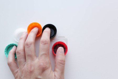 La mano de la mujer sobre cinco tapas de plástico de colores sobre fondo blanco, espacio para la copia. Sostenibilidad, concepto de reciclaje para el 5 de junio Día Mundial del Medio Ambiente