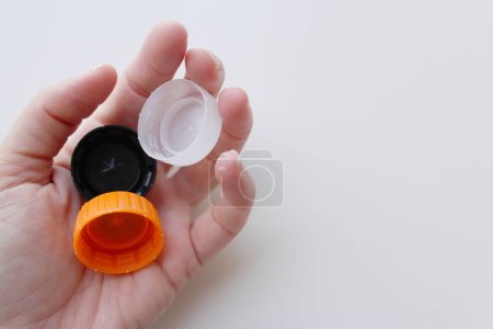 Woman's hand holding three plastic lids on white background, space for copy. Sustainability, recycling concept for June 5th World Environment Day