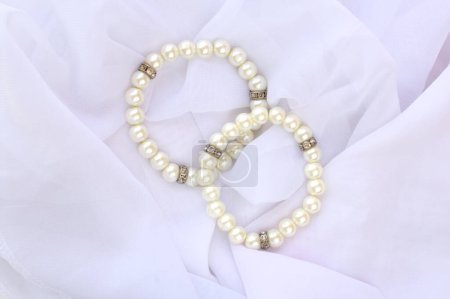 Dos brazaletes de perlas falsas de marfil para llevar de novia. Joyería de moda femenina en la parte superior de tela de velo blanco.