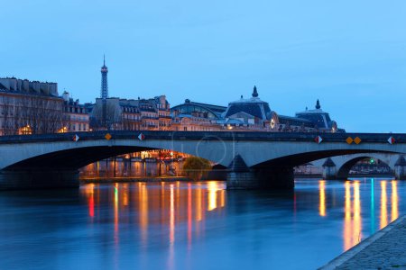 Nachtansicht des Seine-Ufers in Paris, Frankreich, mit Karussellbrücke, Ouay Voltaire und schönem Himmel und Spiegelungen