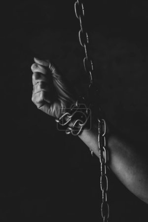 Hand of person chained on black background in studio, feeling lack of freedom, prison