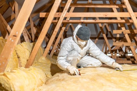 Téléchargez les photos : A man insulates the roof and ceiling of the house with glass wool - en image libre de droit