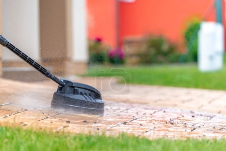Téléchargez les photos : Machine à nettoyer la chaussée en béton devant la maison avec une brosse. Photo de haute qualité - en image libre de droit