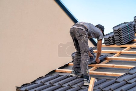 Photo for Roofer installs a fired ceramic tile on the roof. - Royalty Free Image