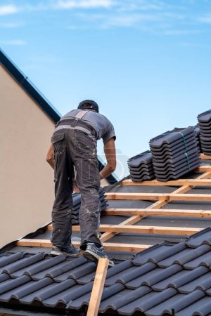 Téléchargez les photos : Travailleur de la construction installe une tuile de céramique cuite sur le toit. - en image libre de droit