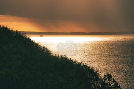 Photo for On the coast of Hundested. Sun rays breaking through the dramatic sky through the clouds at sunset. Mountain with trees in the foreground. Landscape shot in Denmark - Royalty Free Image