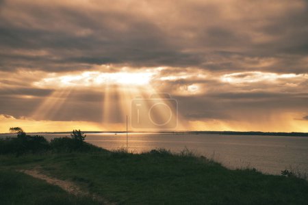 Photo for On the coast of Hundested. Sun rays break through the dramatic sky through the clouds. Meadow with path in foreground. Landscape shot in Denmark - Royalty Free Image