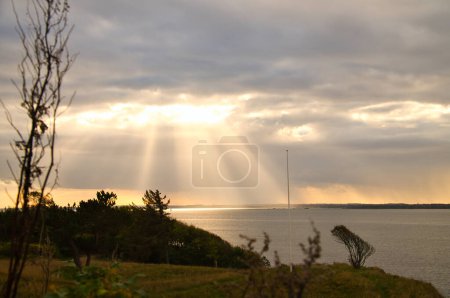 Photo for On the coast of Hundested. Sun rays break through the dramatic sky through the clouds. Meadow in the foreground. Landscape shot in Denmark - Royalty Free Image