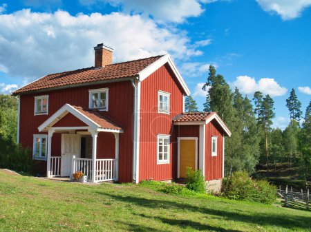 una típica casa sueca roja y blanca en Small and. prado verde y cielo azul con pequeñas nubes. Paisaje de Escandinavia