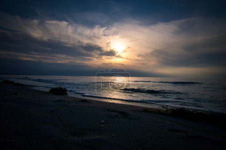 Sunset, illuminated sea. Sandy beach in the foreground. Light waves. Baltic Sea. Landscape on the coast