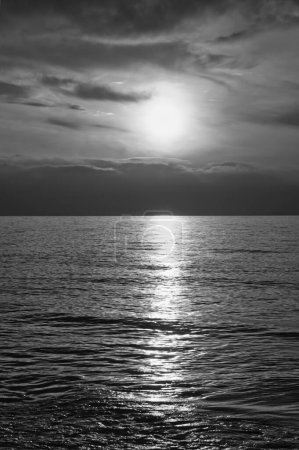 Sunset, illuminated sea in black and white. A few clouds in the sky, light waves rolling towards the Baltic Sea beach. Landscape on the coast