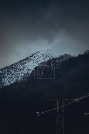 Dark and moody scenery of a snowy mountain with dark clouds above.