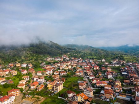 Bulgaria - 05 22 2024: Flying with the Dji mini 2 drone over a village capturing the light hitting the houses with fog coming down from the mountain on the left and beautiful cloudy sky in the back.