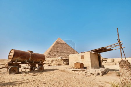 Foto de Giza, Egipto - 24 de diciembre de 2023: Pirámide de Khafre (también conocida como Khafra, Khefren) en la meseta de Giza, el petrolero oxidado, el camión cisterna y el cobertizo de adobe - Imagen libre de derechos